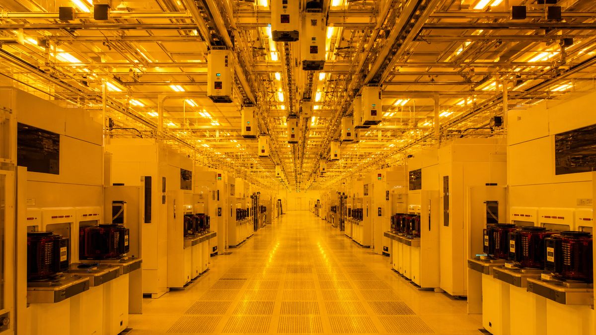 Rows of wafer processing equipment in a bright semiconductor cleanroom with yellow lighting and no people visible